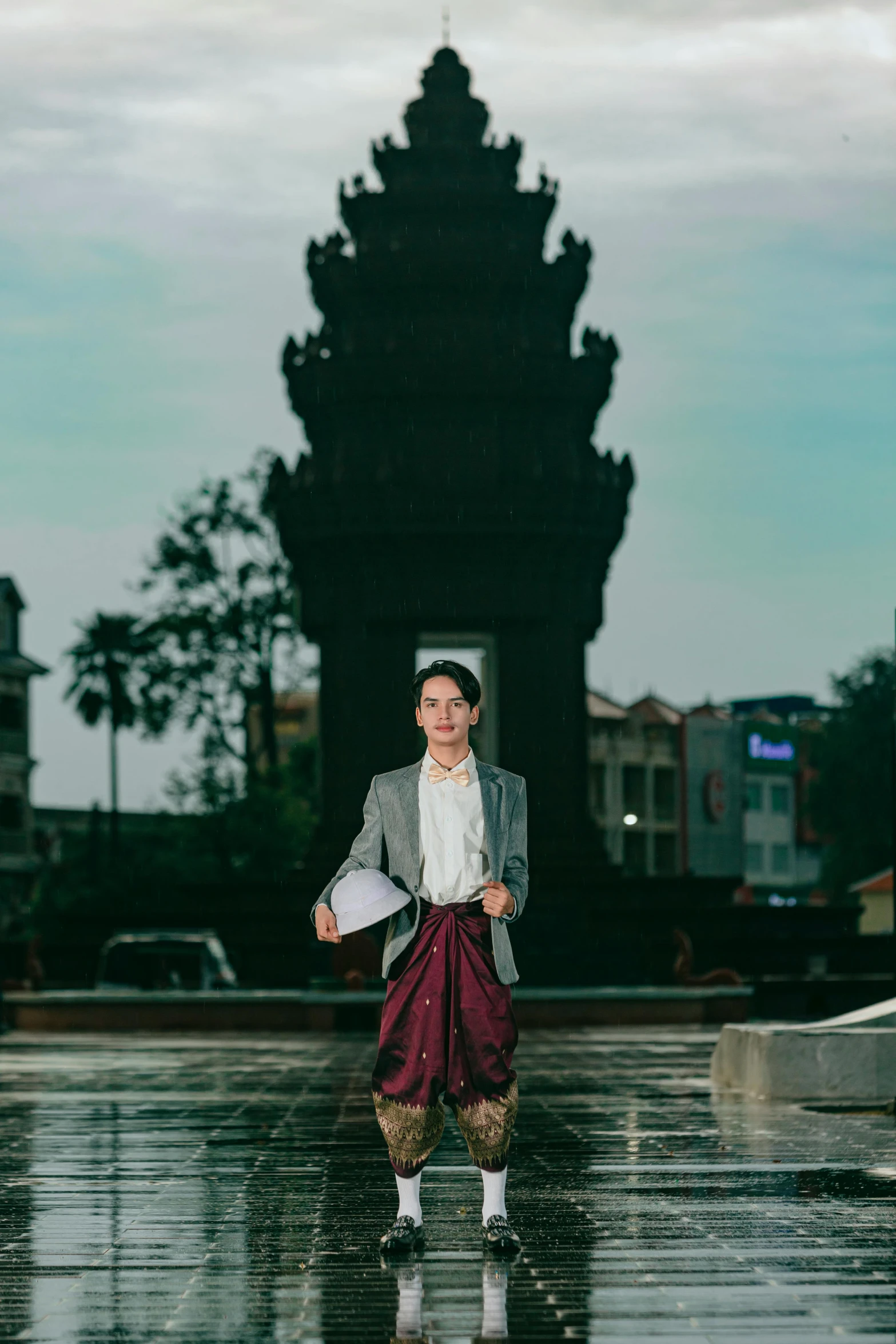 a woman in a white shirt, gray blazer and pink skirt walks on wet pavement