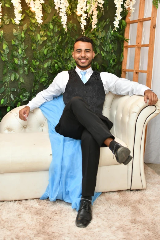 a man sits on top of a white couch wearing a tie