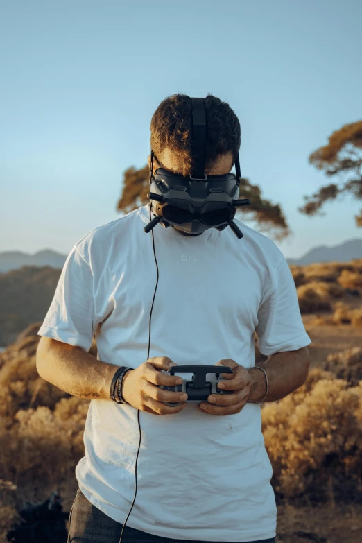 a person with ear phones, standing in some grass with one hand holding a game controller