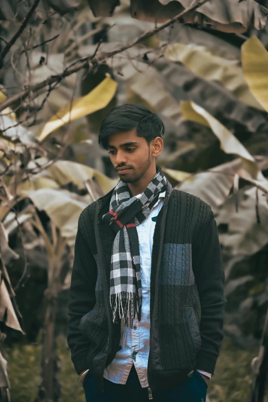 young man in scarf and jacket standing with trees in background