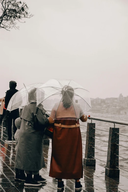 people standing in the rain on a rainy day, while one person holds a clear umbrella