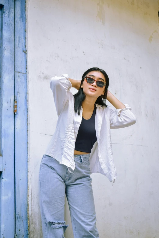 a young woman standing next to a wall wearing sunglasses