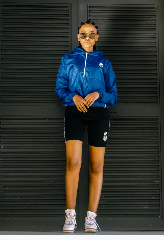 a girl standing against a wall wearing shorts and a blue jacket