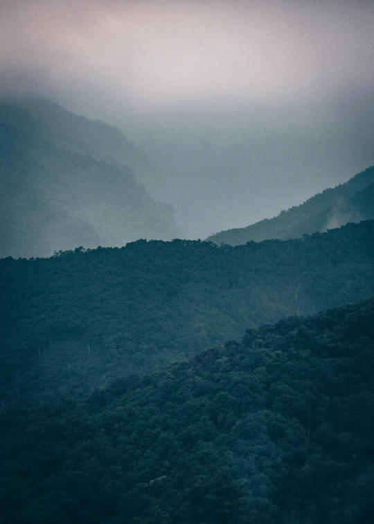 a dark green field next to a mountain under cloudy skies