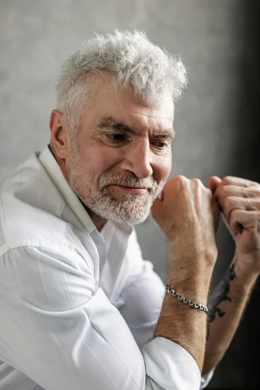 an older man with white hair smiles and holds his hands in his pockets