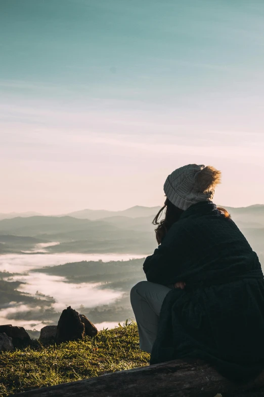 two people sitting on a rock looking out over a valley