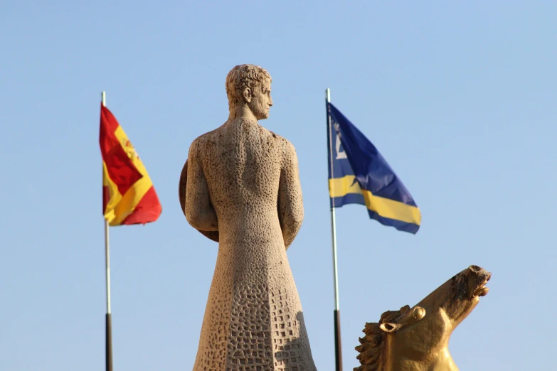 the statues of two men and two horses stand on a hilltop near flags