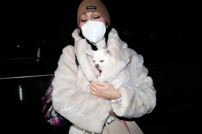 a woman wearing a face mask holds her small white dog