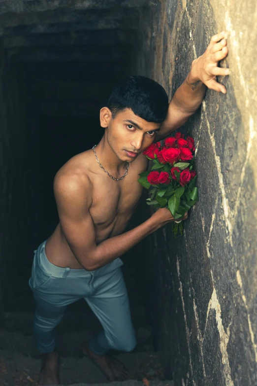 a young man leaning on a wall with red roses in his hand