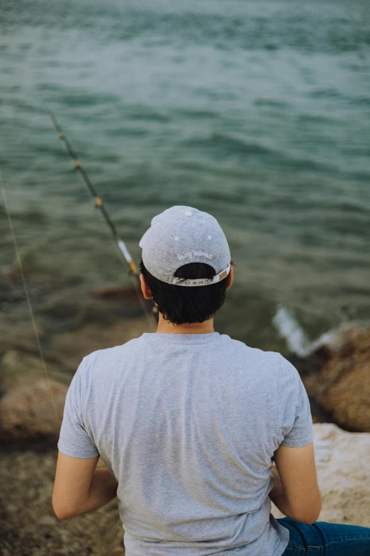 a young man is sitting and fishing on the rocks by the water