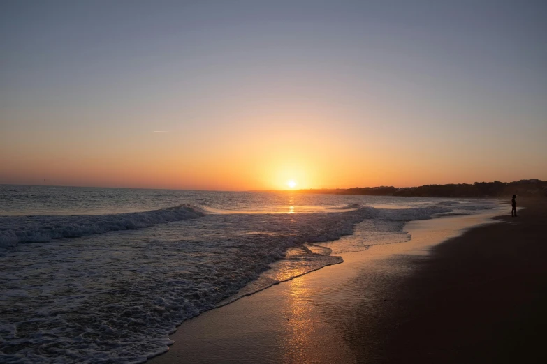 the sunset is setting over the ocean as people walk on the beach