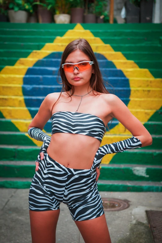 woman in swimsuit standing against wall wearing sunglasses