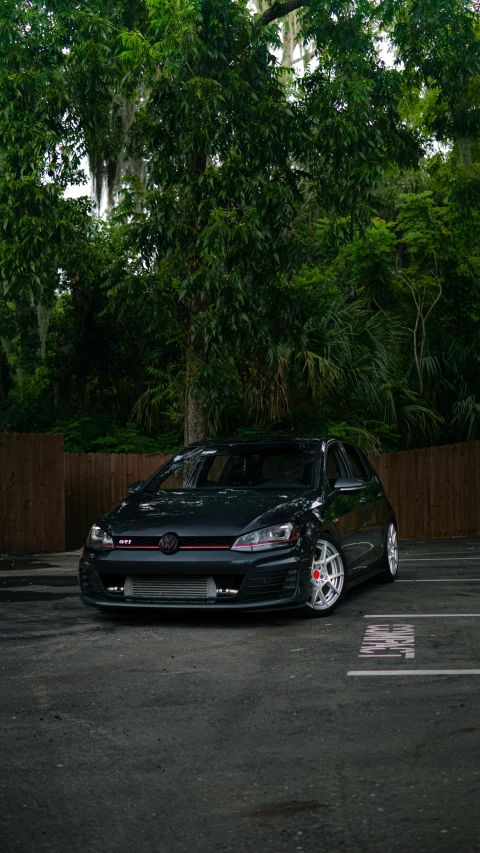 a black car parked in a lot with trees around