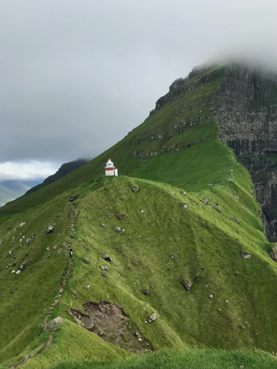 a small cabin sitting on the side of a green mountain