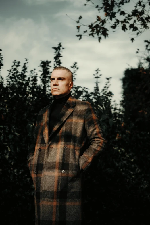 a man in a checkered coat is standing by bushes