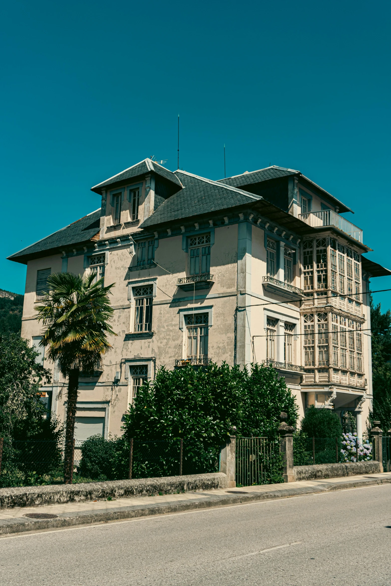 an old building on the side of a street with a fence and palm trees