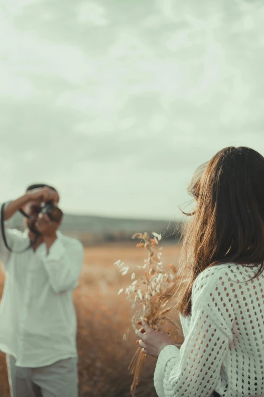 a man standing in a field with a woman holding a camera up