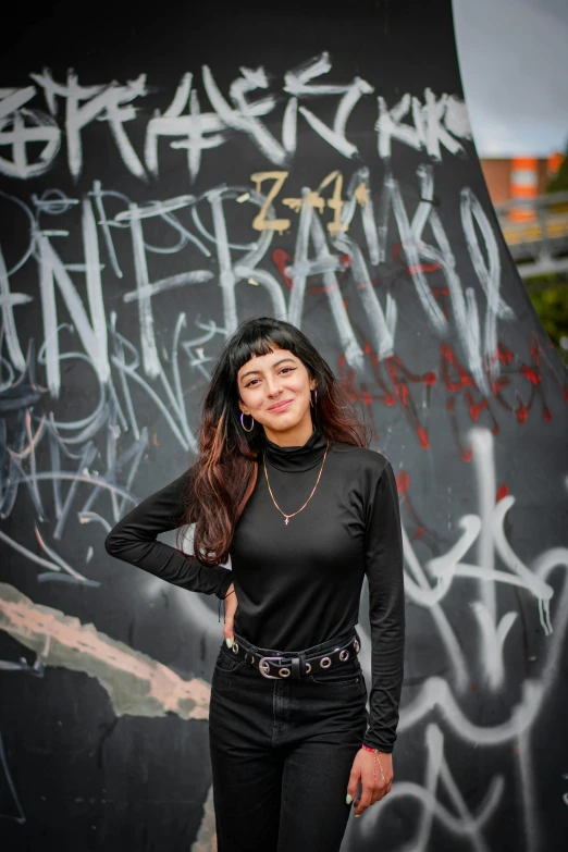 woman standing next to a graffiti wall posing for a po