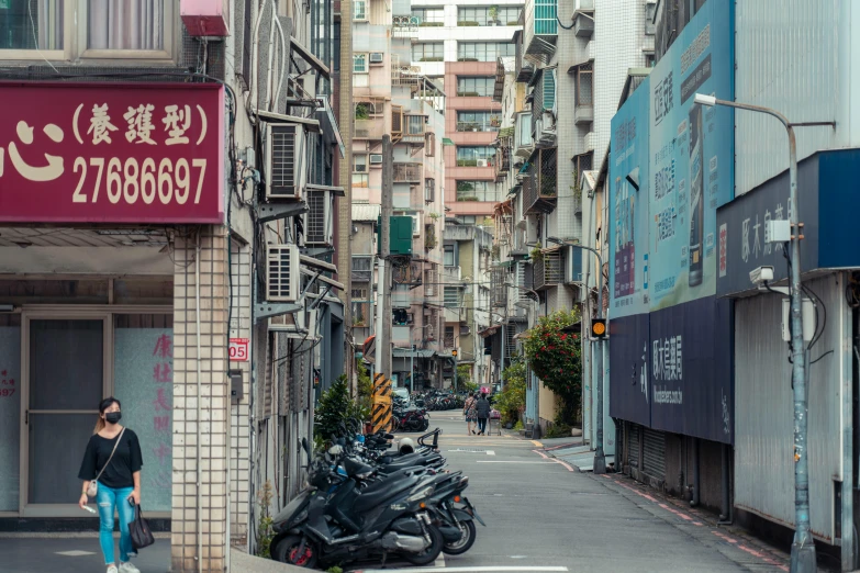 two motorcyclists walk on a narrow street in an asian city