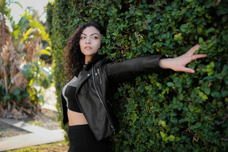 a young lady poses for the camera leaning against a shrub