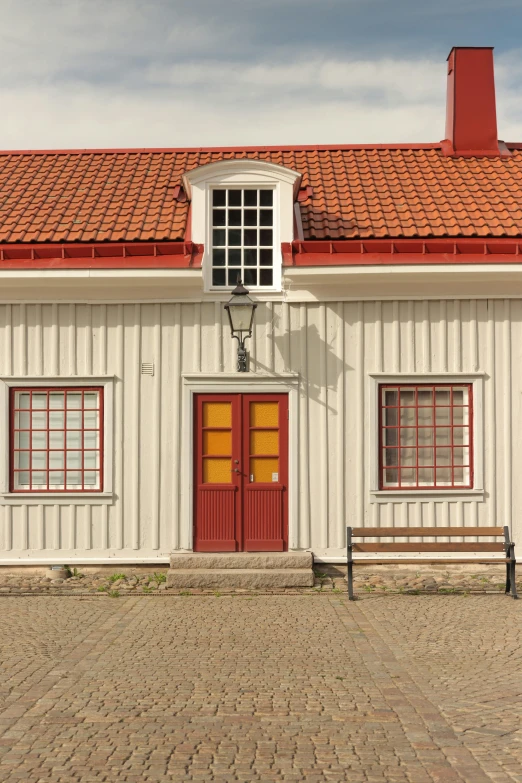 there is a small white building with red trim and a bench in front