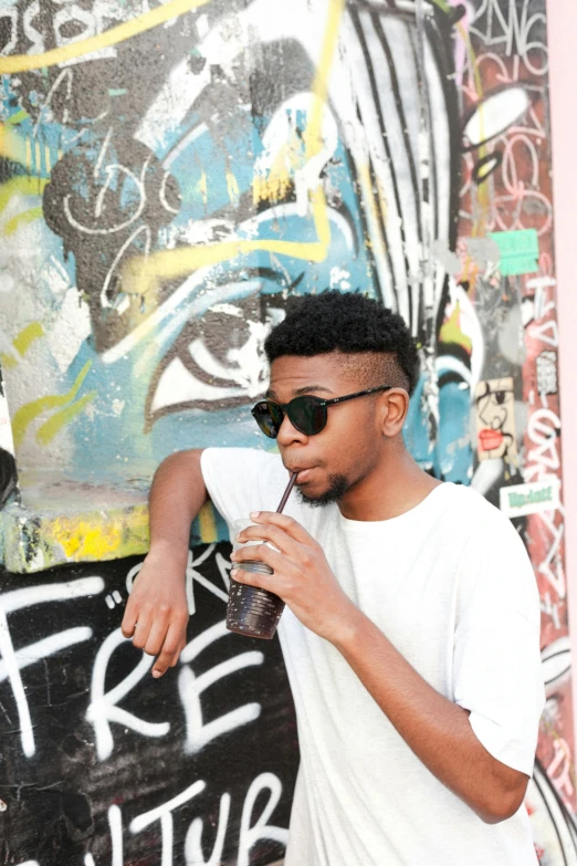 young man drinking a glass of soda in front of a graffiti - covered wall