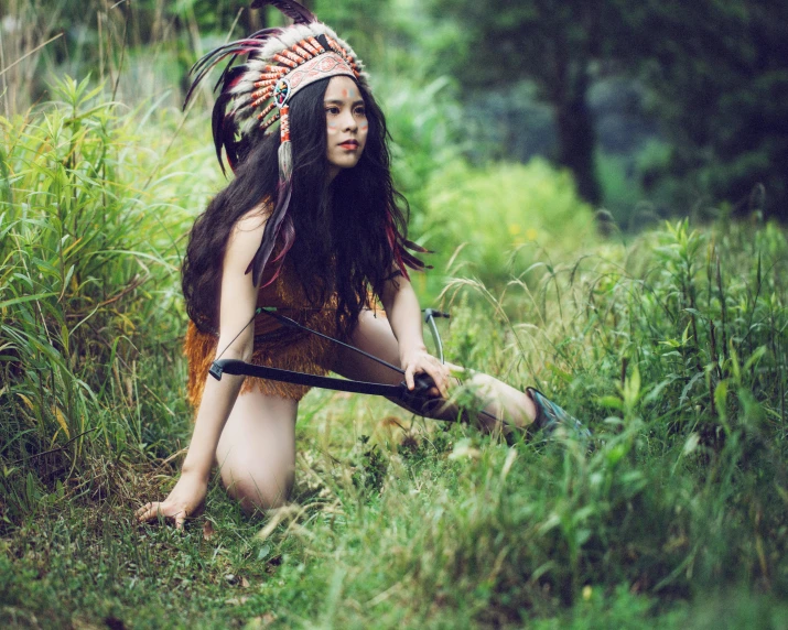 an indian woman kneeling in the woods with her bow