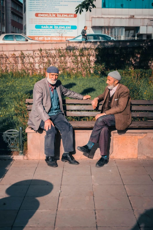 two people sitting on a park bench, one man holding a fist