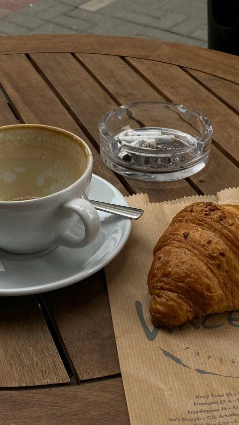 an arm holding coffee and a croissant on a table