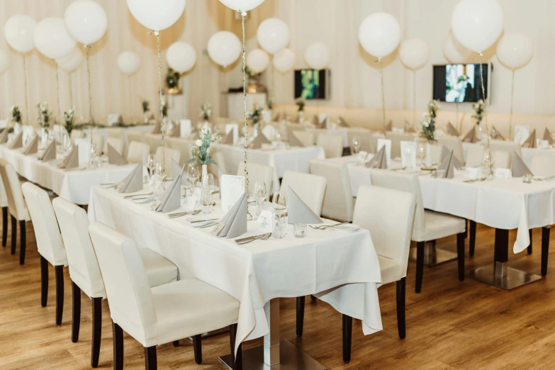 several tables covered in chairs and white table cloths with clear and silver vases