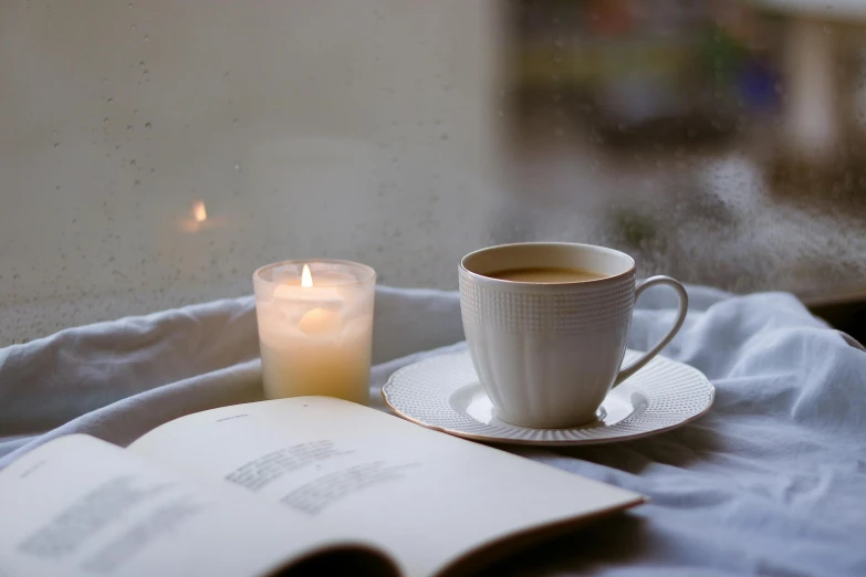 a cup of coffee sits on a saucer and looks out of the window, next to a candle