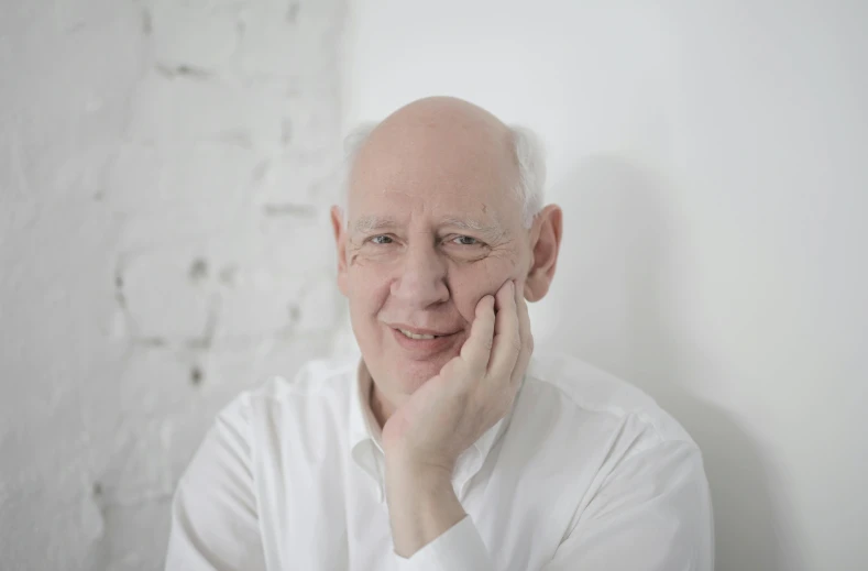 man smiling in front of white brick wall