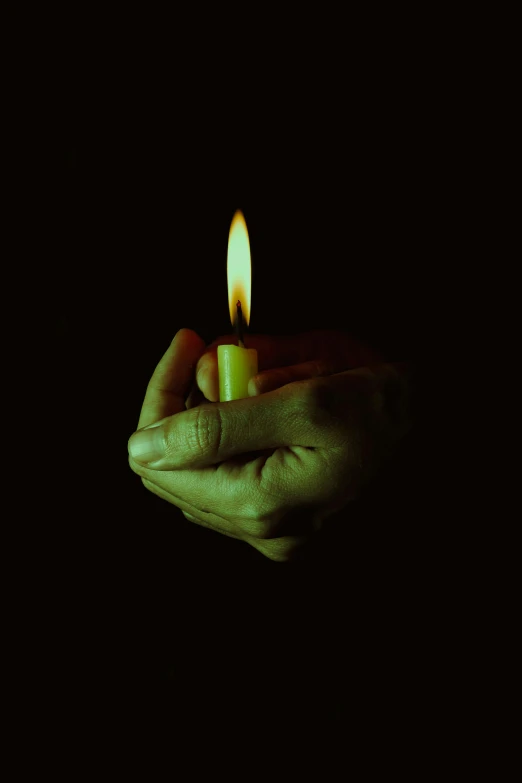 a hand holding a small lit candle on a dark background