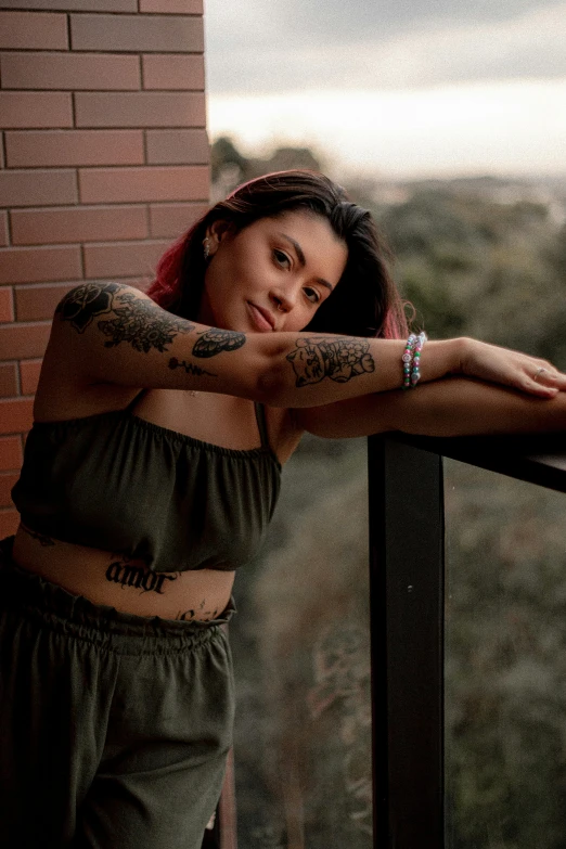 a woman with tattoos and arm sleeves leans against a balcony