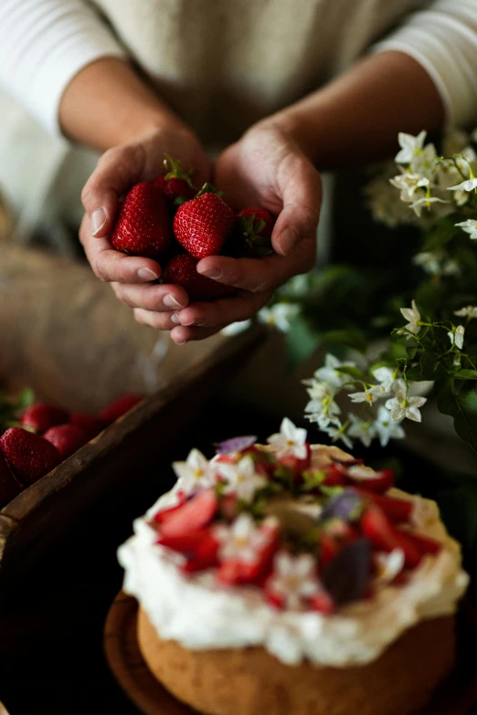 someone reaching for some strawberries to put on top of cake