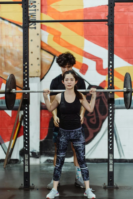 a woman lifting a bar with a man standing behind her
