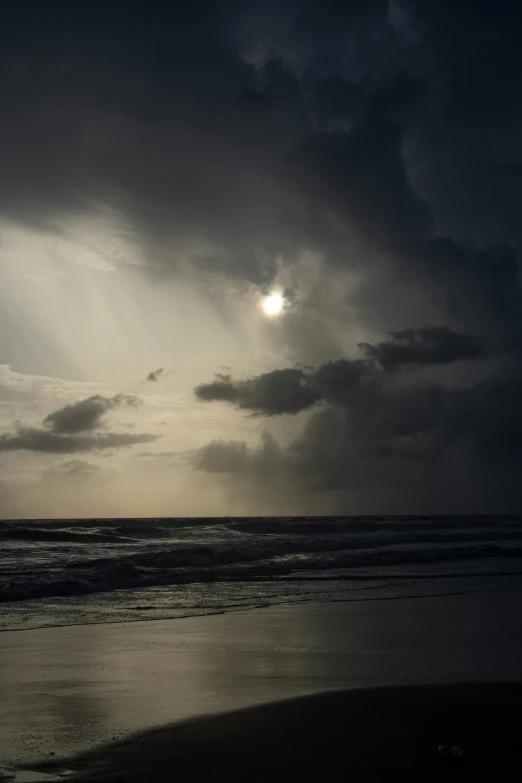 a beach view under dark clouds with the sun shining through it