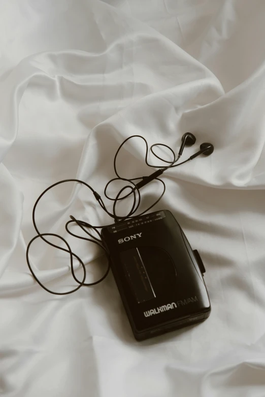 the black mp3 player is laying on white sheets