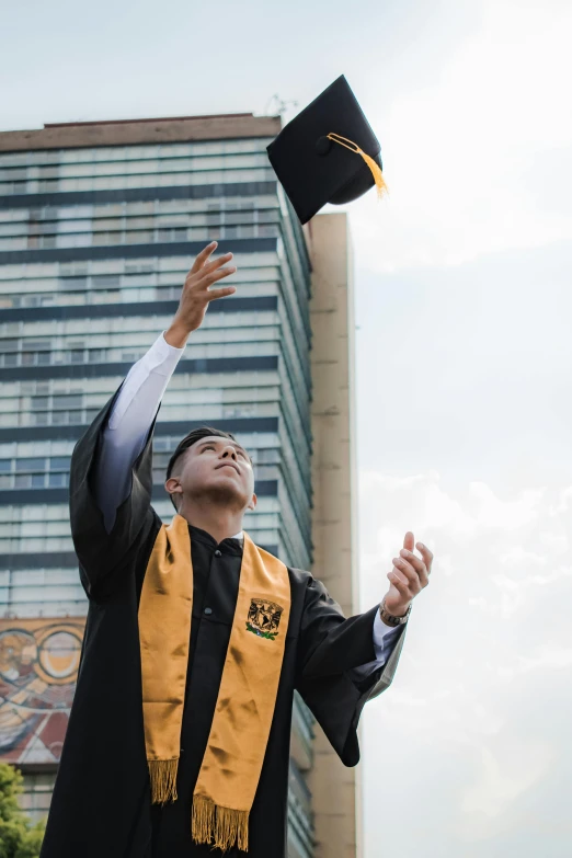 a young man in graduation regalis raises his hat in the air