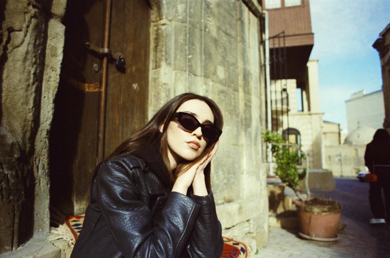 woman with sunglasses posing for a po while leaning against the wall