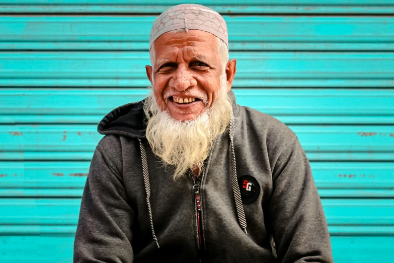 an old man with a beard sits in front of a blue garage door