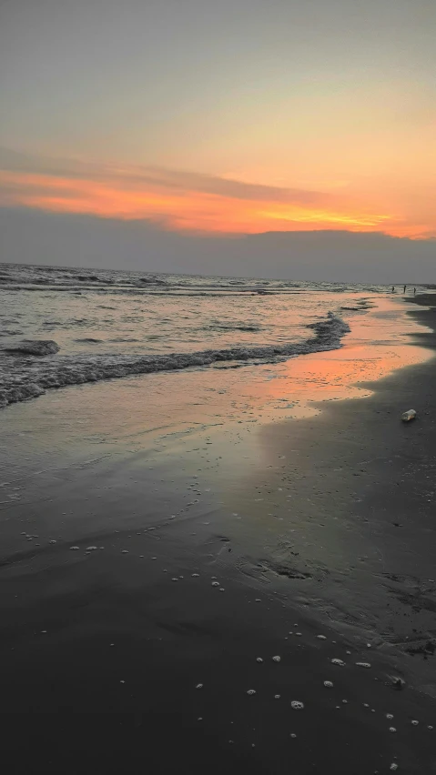 the ocean shore has a body of water with a colorful sunset in the distance