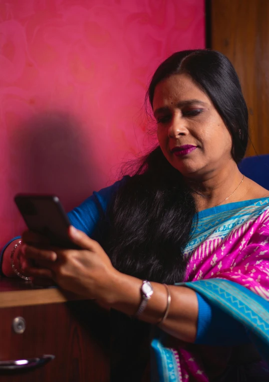 a woman with long dark hair and a pink wall holding her cell phone