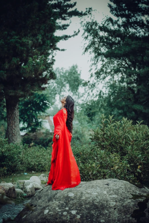 there is a woman in a long red dress by some rocks