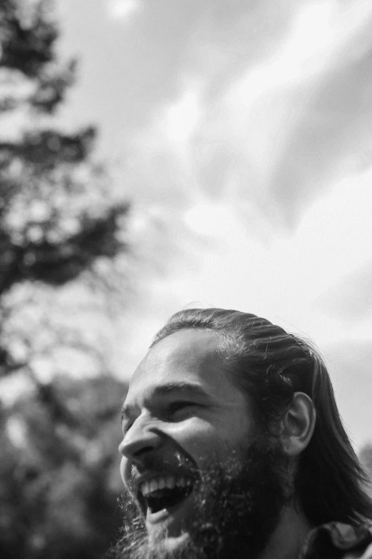 a bearded man is laughing while standing in front of trees