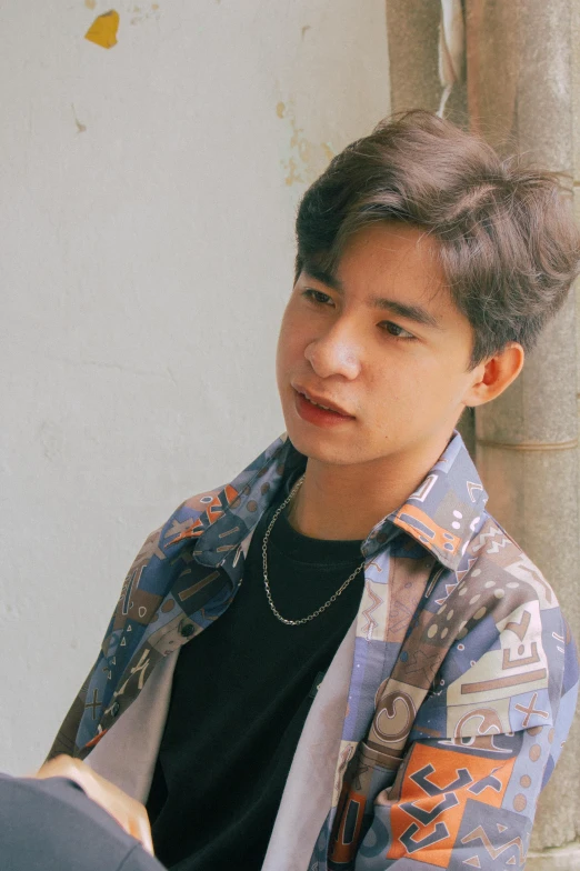 a young man wearing a black shirt has a blue and orange floral jacket