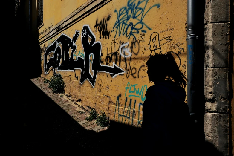 a person in shadow walking near some graffiti covered walls