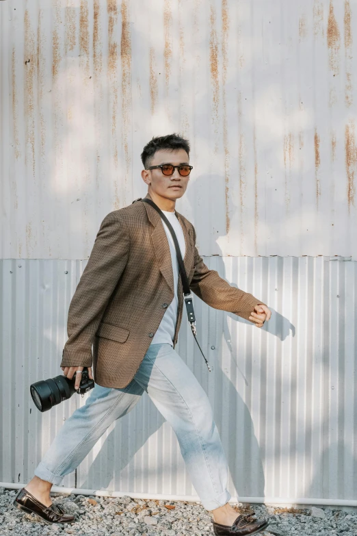 a man with brown coat and sunglasses and a black camera in hand