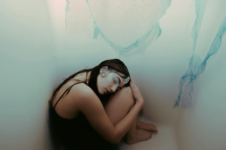 a young woman sitting in a bathtub with a face drawn on the wall