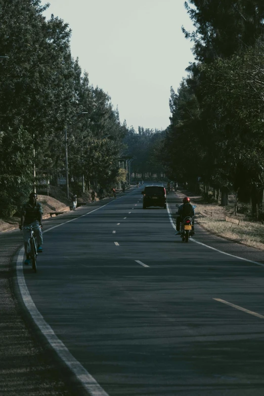 two motorcyclists riding down a road near parked cars